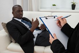 african_patient_sitting_couch_female_psychiatrist_writing_cg9p5586776c_th